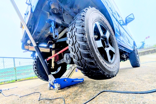 青いフロアジャッキでジャッキアップされたジムニーJB23のリア下回り。赤いラテラルロッドが見える。